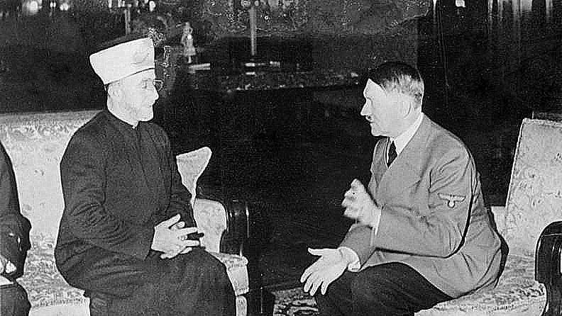 Cette image montre deux hommes assis dans une pièce. L'un d'eux porte un habit traditionnel avec un couvre-chef, tandis que l'autre est vêtu d'un uniforme militaire. Ils semblent être en conversation, gesticulant avec leurs mains. L'environnement est richement décoré, avec des meubles élégants et des éléments de décoration en arrière-plan. L'image évoque un moment de rencontre entre ces deux figures historiques.