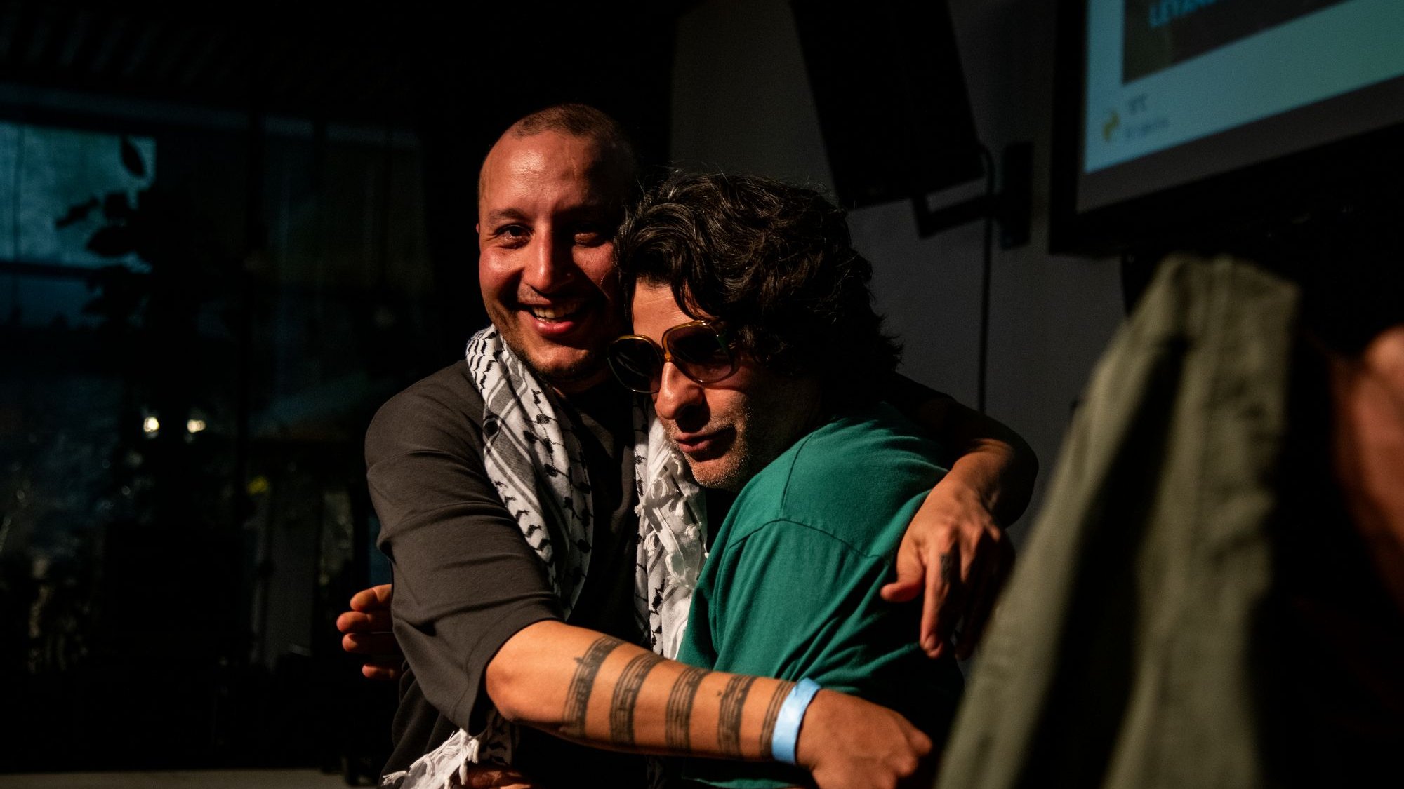 Deux hommes s'étreignent, souriants, avec des déguisements et un ambiance chaleureuse.