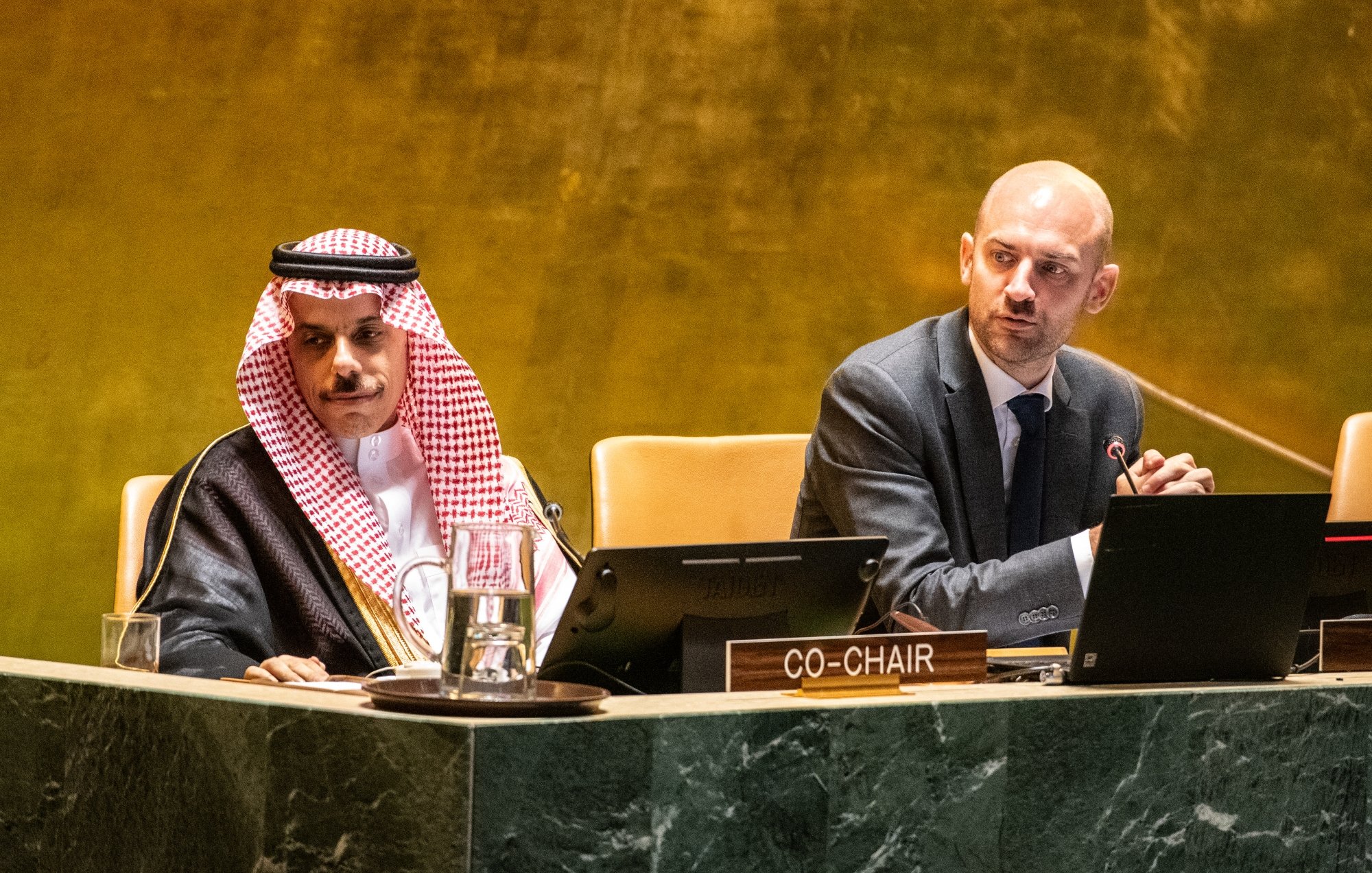 Deux hommes en costume assis à une table dans une salle de conférence.