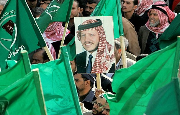 L'image montre une foule rassemblée, tenant des drapeaux verts. Au centre, il y a un portrait d'un homme, probablement une figure importante, qui est mis en avant parmi les drapeaux. L'atmosphère semble être celle d'une manifestation ou d'un rassemblement politique, avec des participants engagés et un message de soutien collectif.