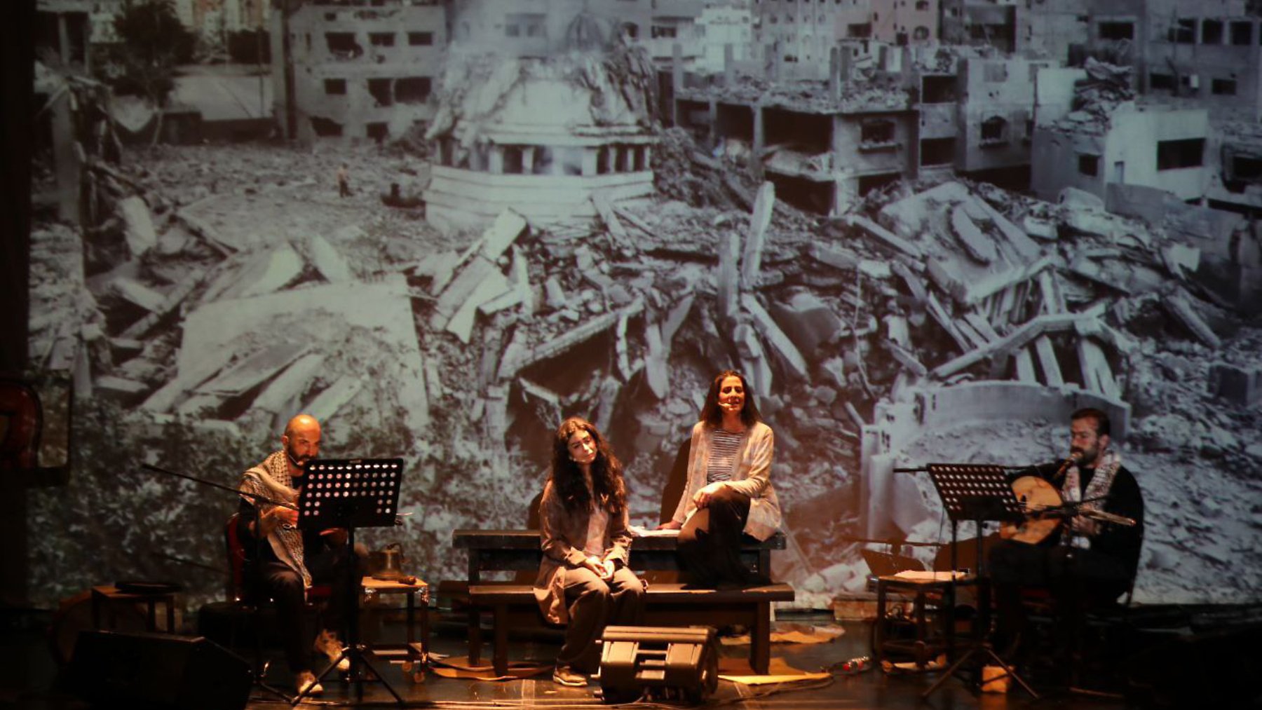Quatre artistes sur scène, avec une projection d'un paysage de destruction en arrière-plan.
