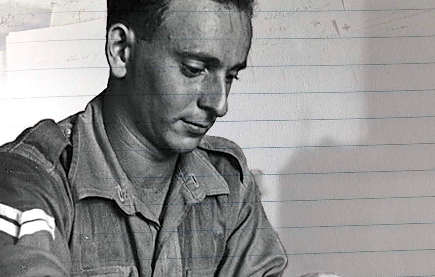 L'image montre un homme en uniforme militaire, concentré sur l'écriture d'une lettre. Il semble pensif, assis à une table et tenant un stylo. Le fond a des éléments flous qui évoquent des documents ou des notes. Cette scène transmet une ambiance de réflexion, peut-être liée à des pensées personnelles ou des nouvelles à envoyer.