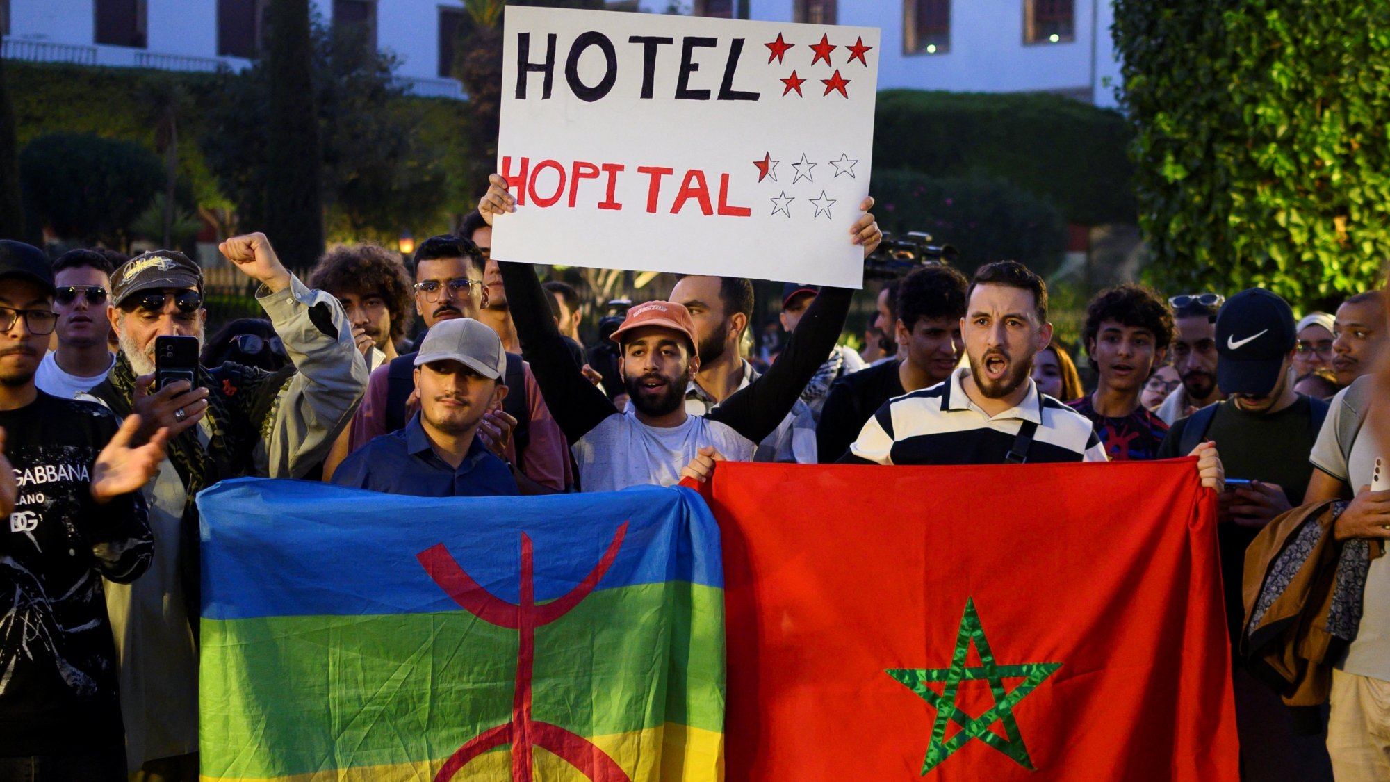 Manifestation avec des drapeaux marocains et amazigh, pancarte pour un hôtel.