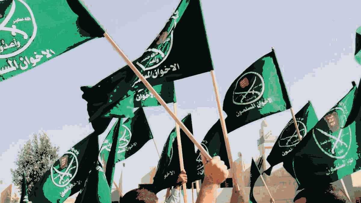 L'image montre un groupe de personnes levant des drapeaux verts. Les drapeaux semblent porter des inscriptions en arabe ainsi que des symboles, indiquant une affiliation à un mouvement ou une organisation spécifique. L'ambiance semble dynamique et engagée, suggérant un rassemblement ou une manifestation. L'arrière-plan indique probablement un espace public ou un lieu symbolique.