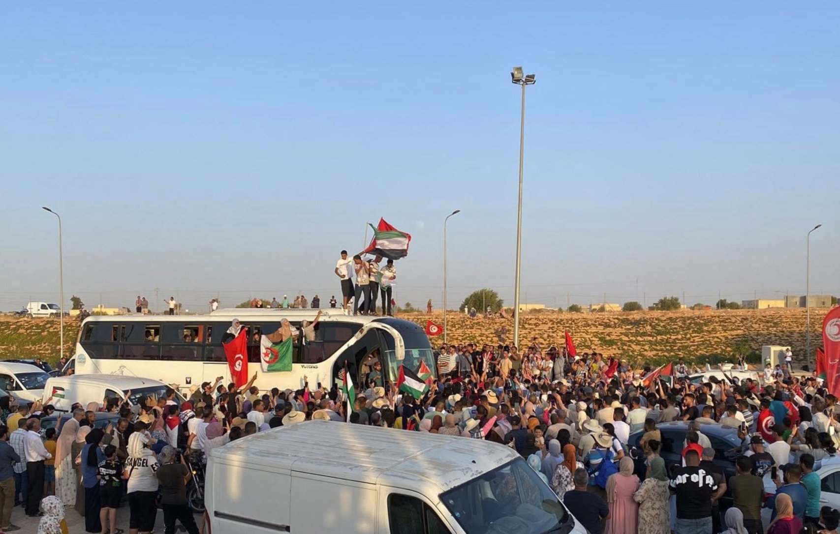 Une foule rassemblée autour d'un bus, brandissant des drapeaux et des pancartes.