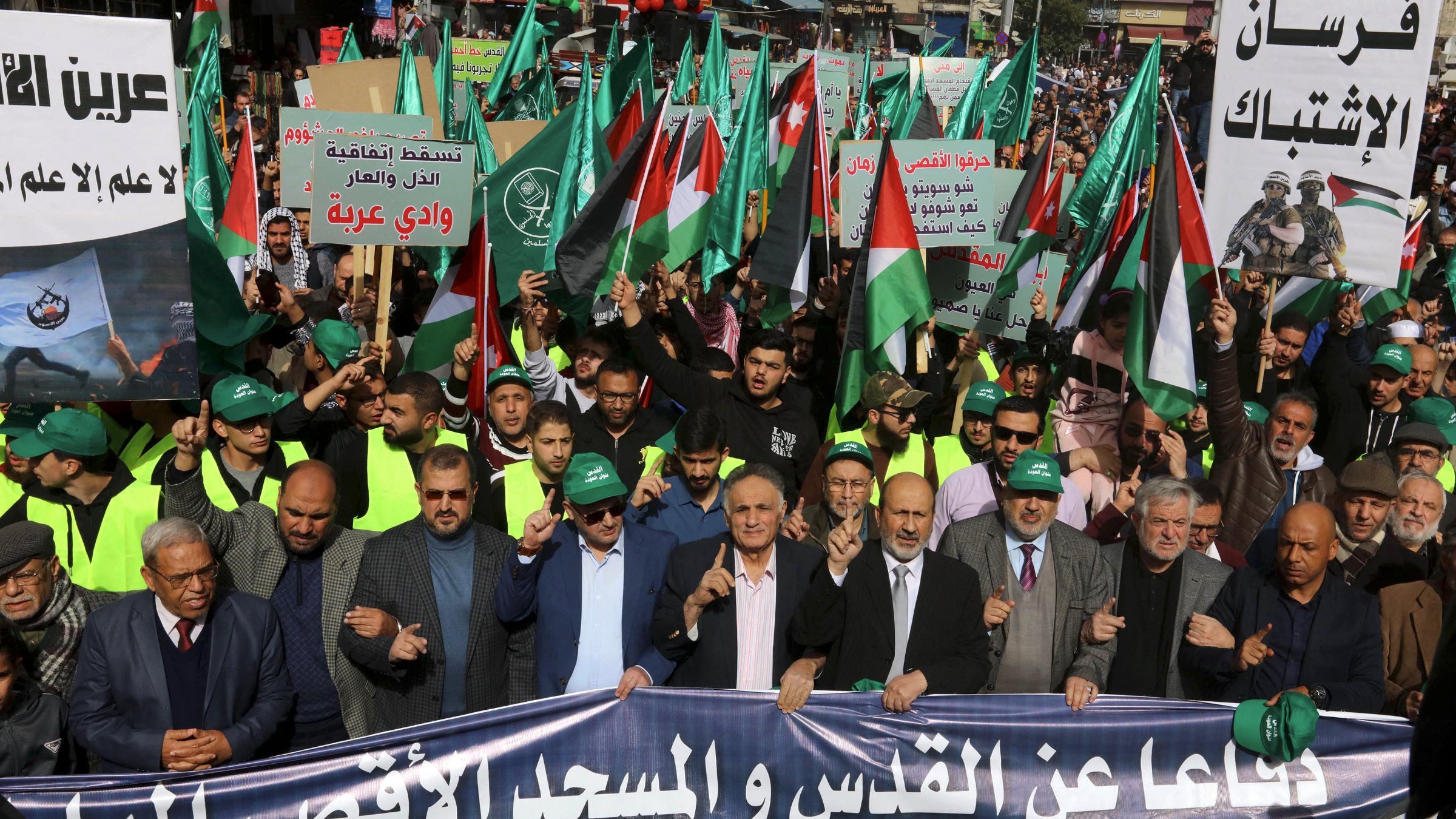 Manifestation avec drapeaux palestiniens, pancartes et participants en vert et noir.