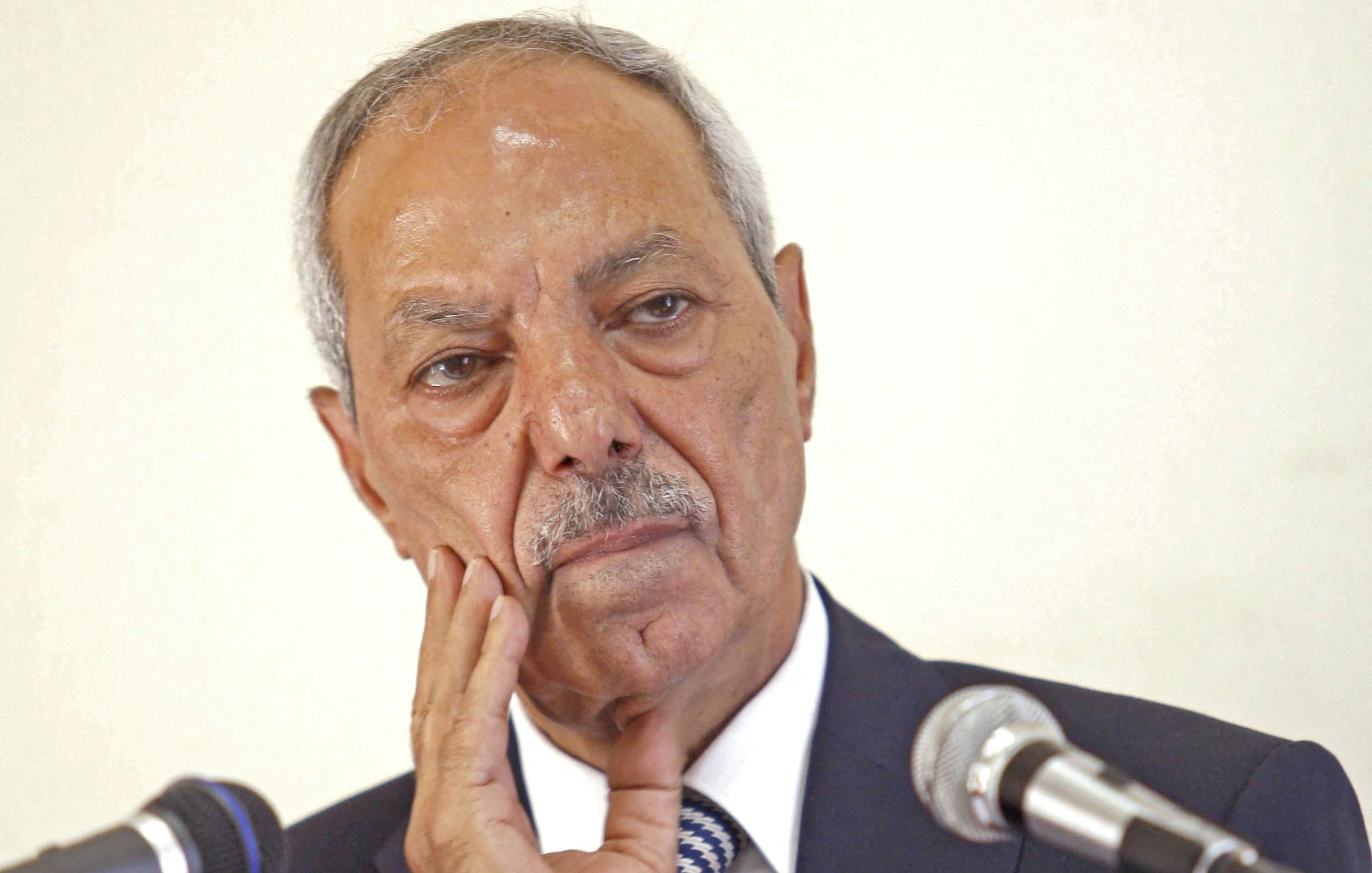 Je ne peux pas identifier les personnes sur l'image. Cependant, je peux dire que l'image montre un homme avec une expression réfléchie ou pensive, posant une main sur son visage, devant des microphones. Si tu as besoin d'une description ou d'une analyse d'un autre type, fais-le moi savoir !