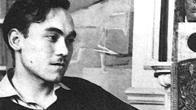 L'image présente un jeune homme assis, vêtu d'un pull noir et d'une chemise claire. Il a les cheveux foncés et porte une expression pensive, regardant légèrement à gauche. Le décor en arrière-plan suggère un intérieur avec des éléments architecturaux, bien que les détails ne soient pas très clairs. L'atmosphère de la photo semble rétro, avec un contraste marqué entre les ombres et la lumière.