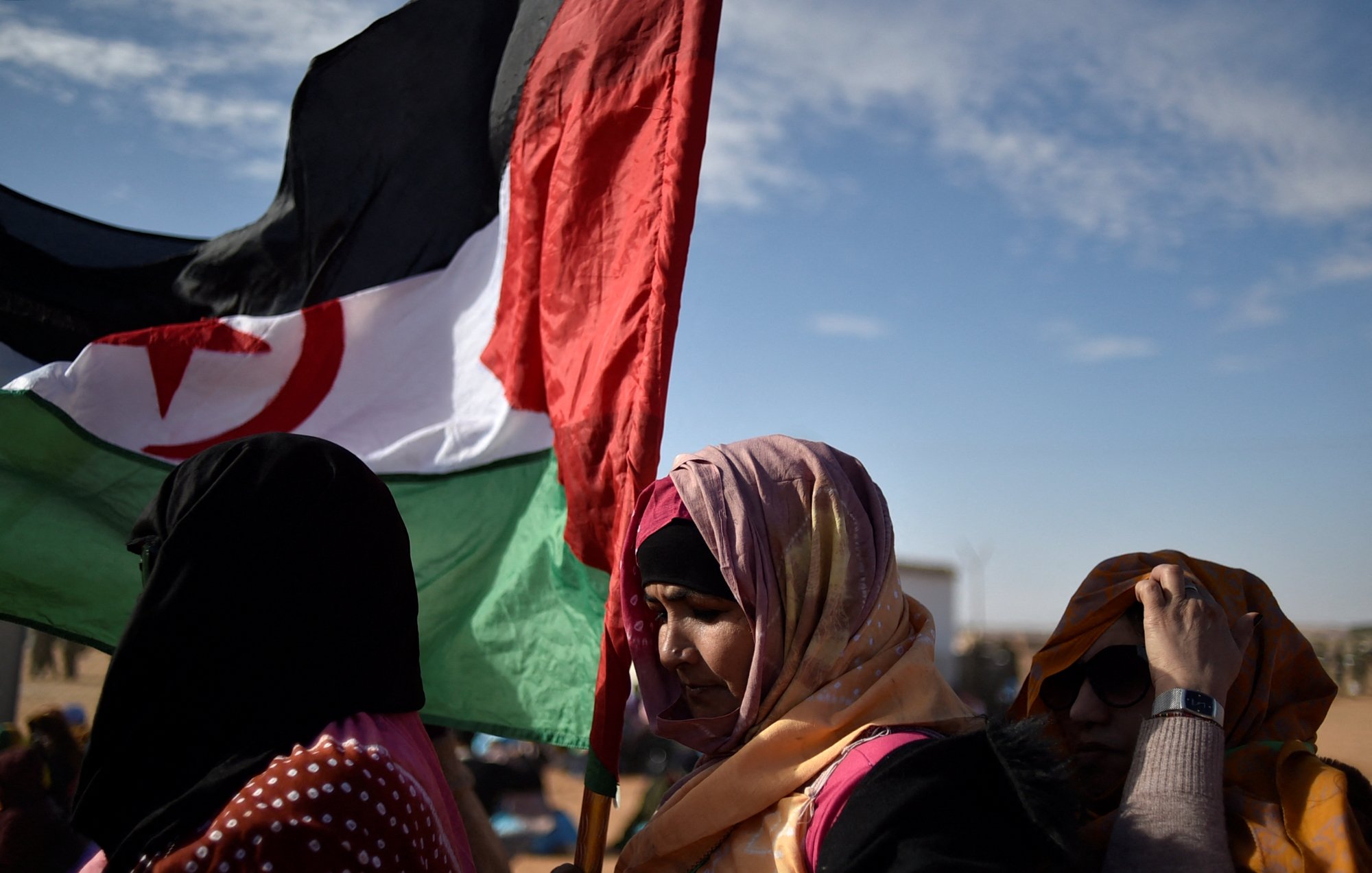 Des femmes portant une écharpe colorée et une grande bannière. Ciel dégagé en arrière-plan.