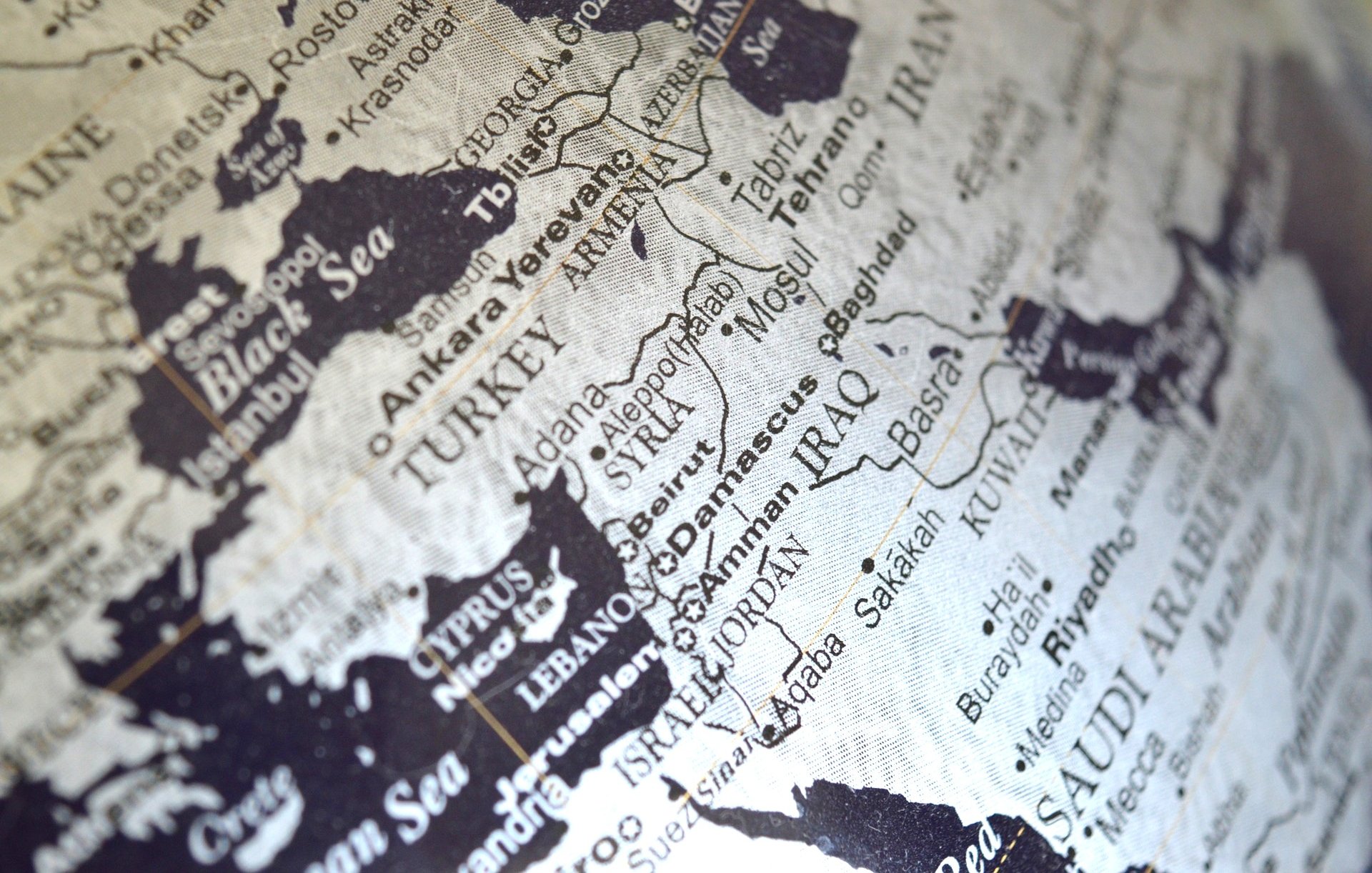 L'image montre une carte en noir et blanc d'une région qui inclut le Moyen-Orient et certaines parties de l'Europe et de l'Asie. On peut distinguer des pays comme la Turquie, l'Iran, l'Irak et l'Arabie Saoudite. Les noms des villes et des pays sont inscrits en lettres claires, créant un contraste avec le fond noir. La carte semble stylisée, donnant une impression de vintage ou d'art graphique.