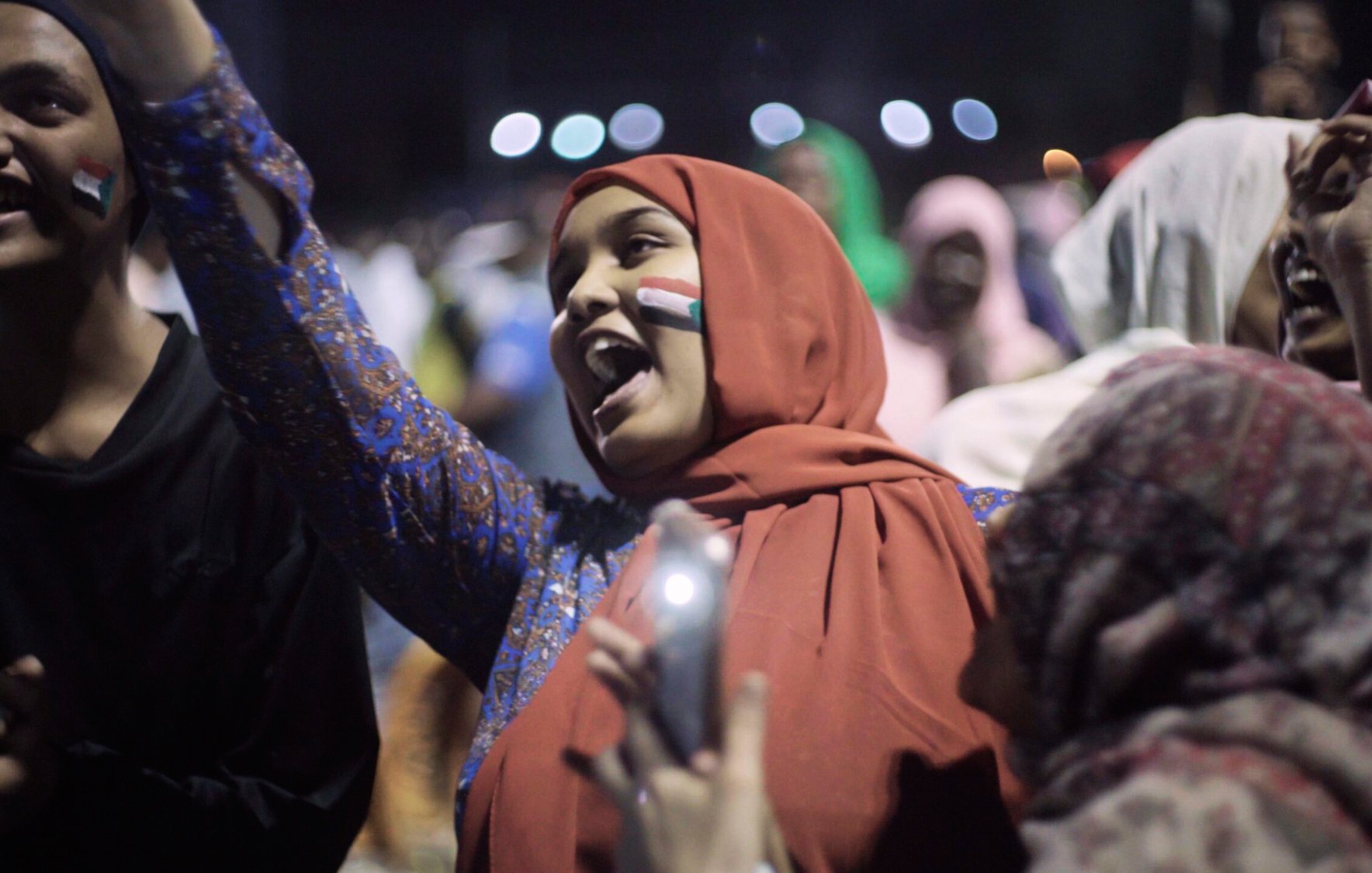 Groupe de jeunes célébrant avec enthousiasme, drapeaux et sourires.