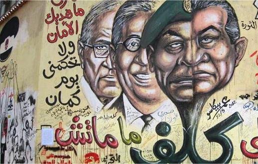 L'image représente une fresque murale avec des portraits de figures politiques, accompagnée de textes en arabe et d'autres éléments graphiques. Les visages semblent se faire face de manière marquante, probablement pour symboliser des conflits ou des idées politiques. Les inscriptions en arabe pourraient évoquer des slogans ou des messages liés à la politique ou à la société. L'utilisation de couleurs vives et de styles artistiques renforce l'impact visuel de cette œuvre.