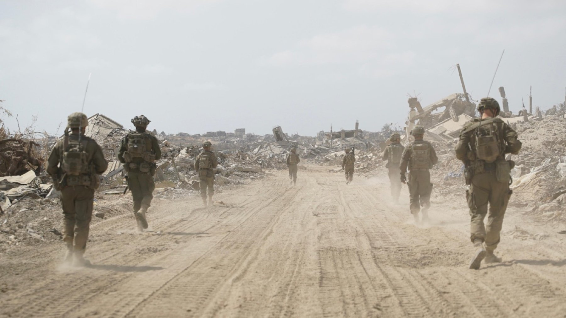 Des soldats marchent sur un chemin poussiéreux, entourés de débris et de ruines.