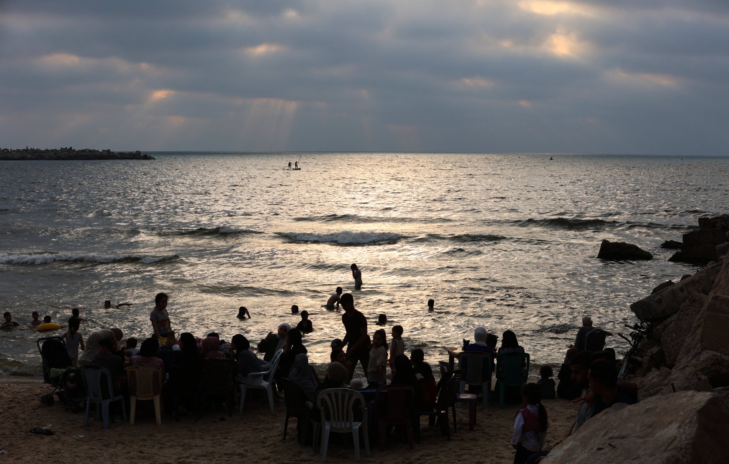 Plage animée au crépuscule, avec des gens dans l'eau et sur le sable.