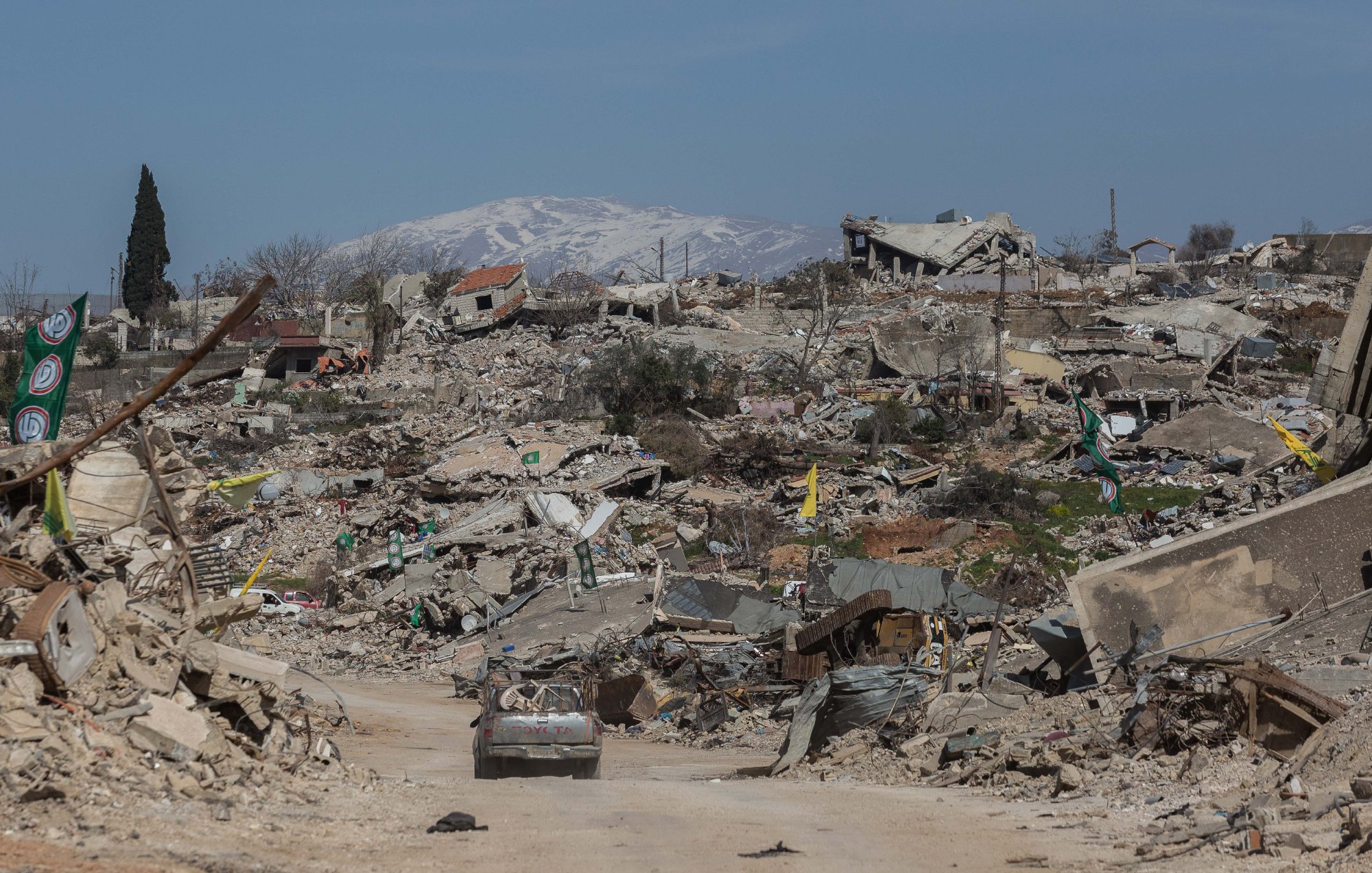 Un paysage dévasté avec des bâtiments en ruines et des montagnes enneigées au loin.