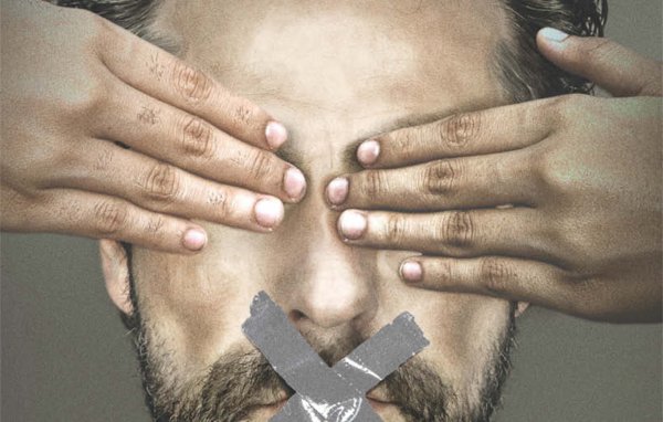 L'image représente un homme avec une barbe qui a les yeux couverts par des mains. Son visage affiche une expression sérieuse et déterminée. Sur sa bouche, il y a une croix qui symbolise le silence, tandis qu'en dessous, on peut lire en lettres majuscules "JOURNALISM IS NOT A CRIME" (Le journalisme n'est pas un crime) et le hashtag "#FREEAJSTAFF". L'ensemble de l'image semble véhiculer un message fort en faveur de la liberté de la presse et de la protection des journalistes.