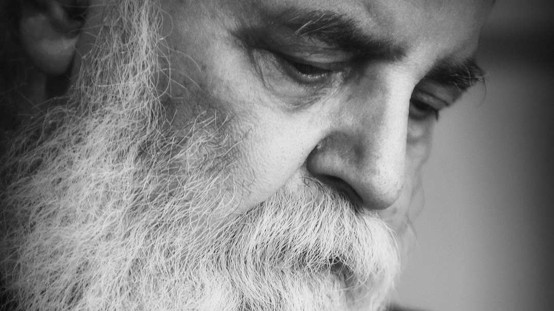 L'image montre un homme âgé avec une longue barbe blanche. Son expression est pensive et introspective, les yeux baissés. L'éclairage est doux, créant un contraste qui met en valeur les détails de son visage et de sa barbe. L'ensemble donne une ambiance de réflexion et de sérénité. La photo est en noir et blanc, ce qui accentue la gravité et la profondeur des émotions.