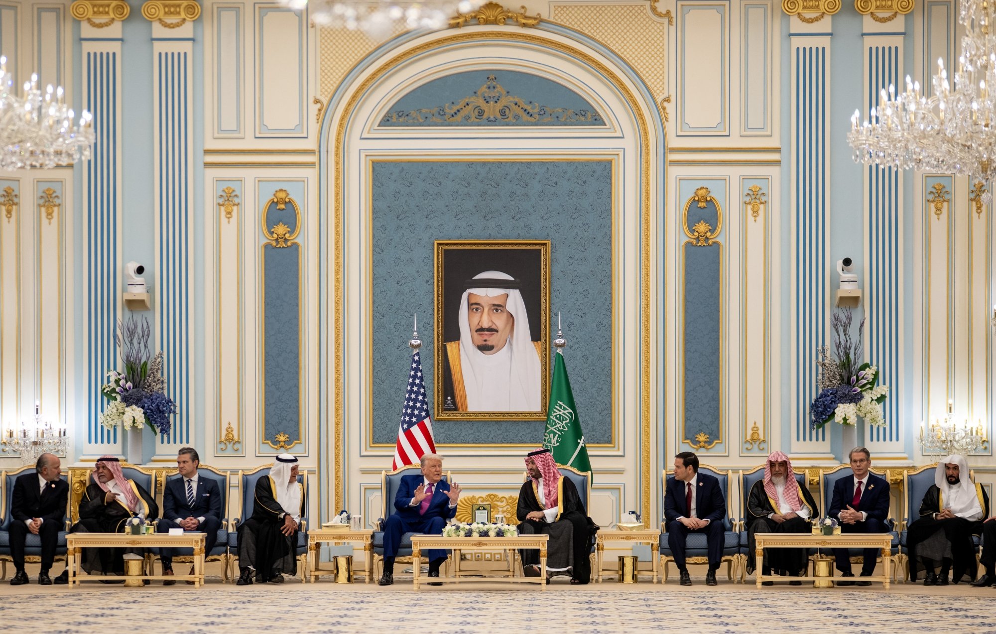 Réunion officielle dans un palais, drapeaux américain et saoudien, hommes en costume autour d'une table.