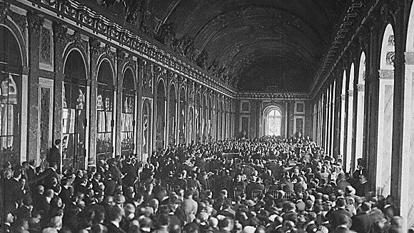 L'image montre une vaste salle intérieure, probablement un palais, remplie d'un grand nombre de personnes. On peut voir des rangées de chaises disposées, et les murs sont ornés de grandes fenêtres et de détails architecturaux. La foule semble rassemblée pour un événement ou une cérémonie importante, créant une atmosphère dense et dynamique dans cet espace majestueux. La lumière pénètre par les fenêtres, ajoutant une ambiance solennelle à la scène.