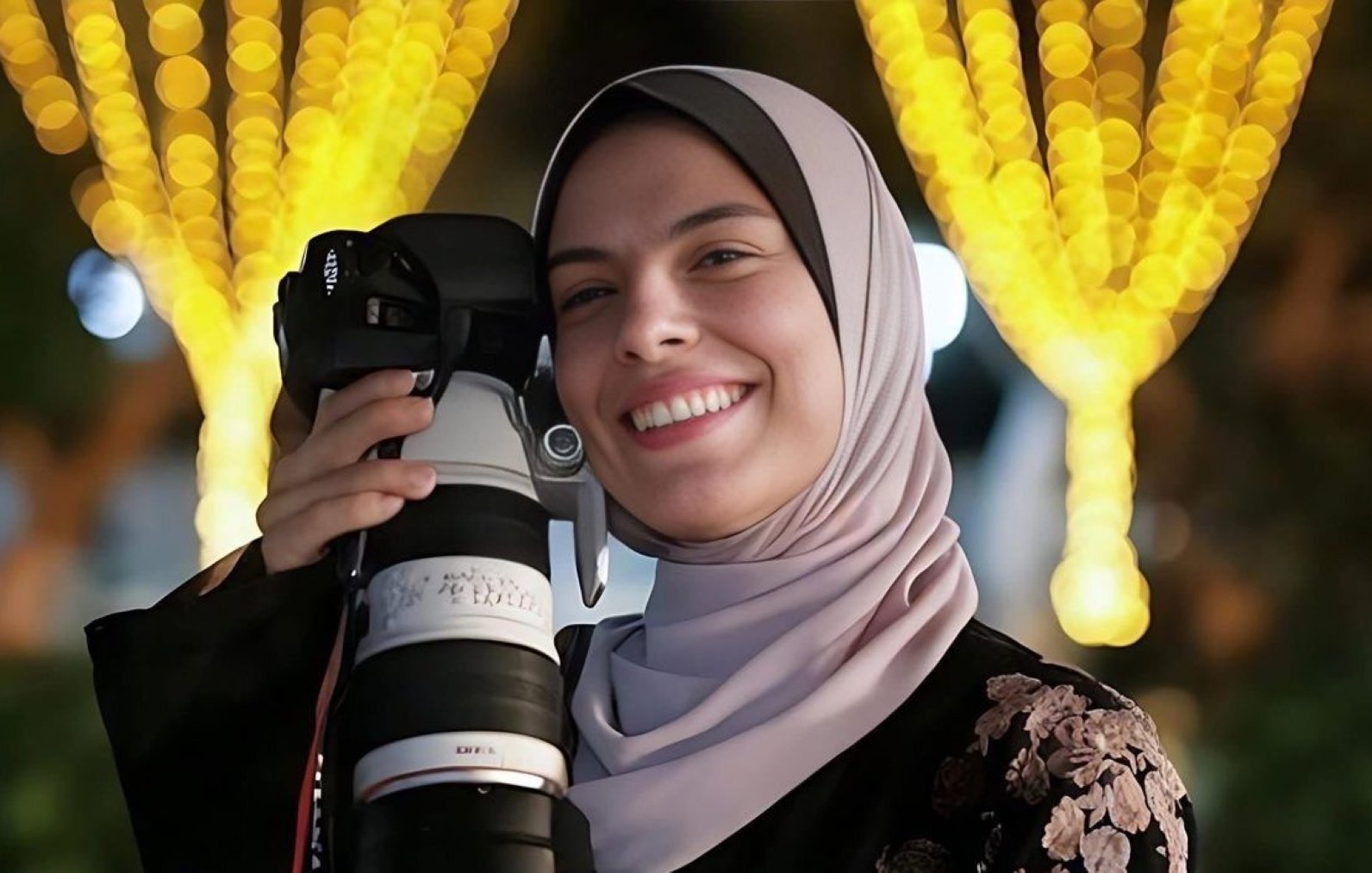 Jeune femme souriante avec un appareil photo, entourée de lumières scintillantes.