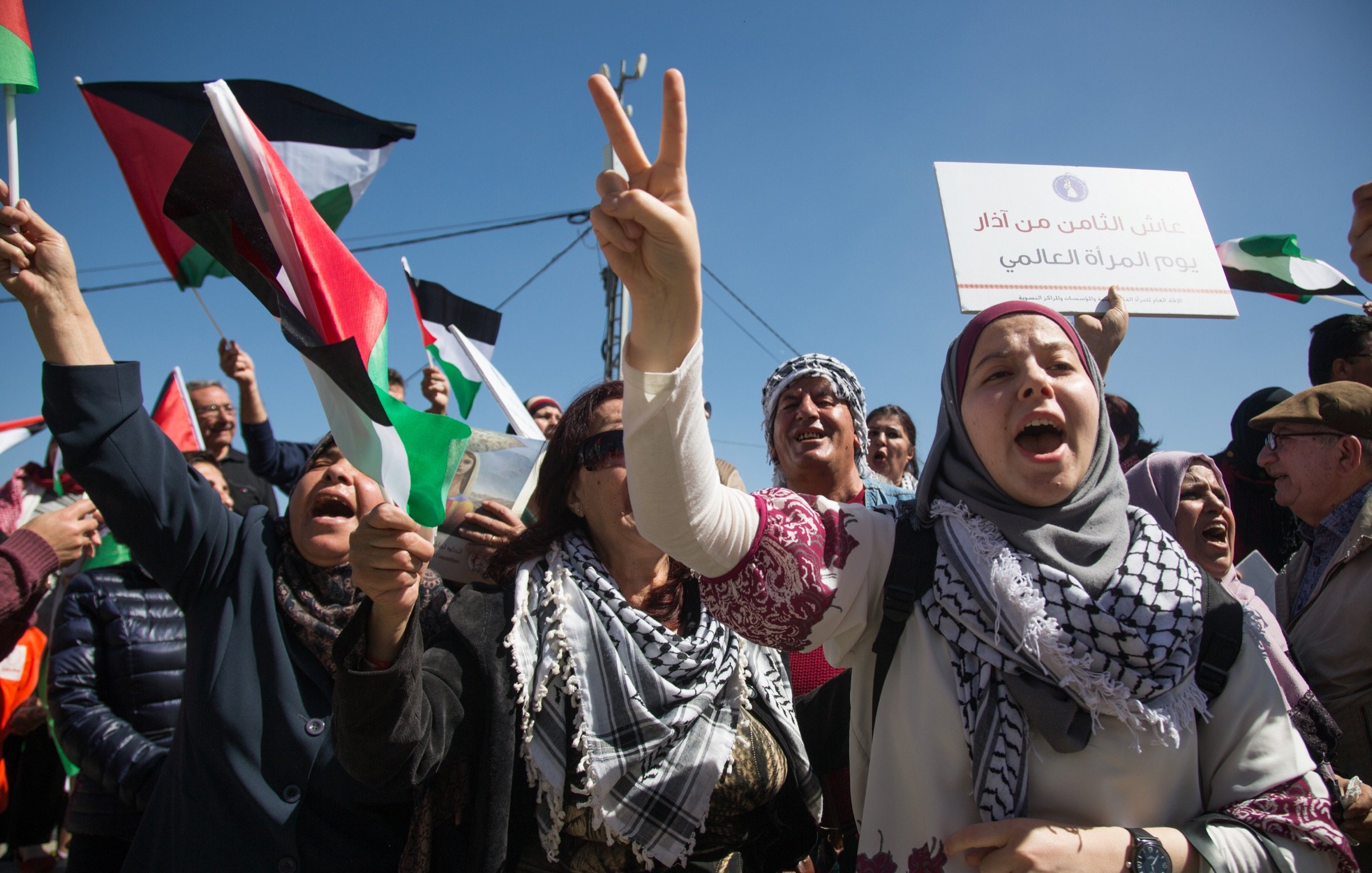 L'image montre une manifestation expressive, avec des personnes brandissant des drapeaux palestiniens et scandant des slogans. Les manifestants semblent passionnés et engagés, certains levant les bras en signe de victoire. Au premier plan, une femme en hijab tient un panneau et exprime son enthousiasme. L'arrière-plan est rempli de supporters, créant une atmosphère de solidarité et de détermination. La scène se déroule sous un ciel bleu, renforçant le sentiment d'énergie et de mobilisation.