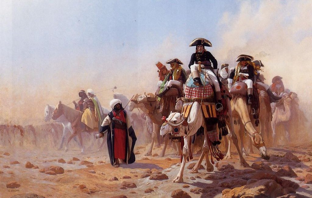 L'image représente un groupe de cavaliers sur des chevaux et des chameaux, se déplaçant à travers un paysage désertique. Les cavaliers portent des costumes traditionnels riches en couleur, souvent ornés de détails. On peut voir de la poussière soulevée par le mouvement, créant une atmosphère de chaleur et d'intensité. L'arrière-plan est flou, suggérant l'immensité du désert. L'ensemble dégage une impression de mouvement et d'aventure.