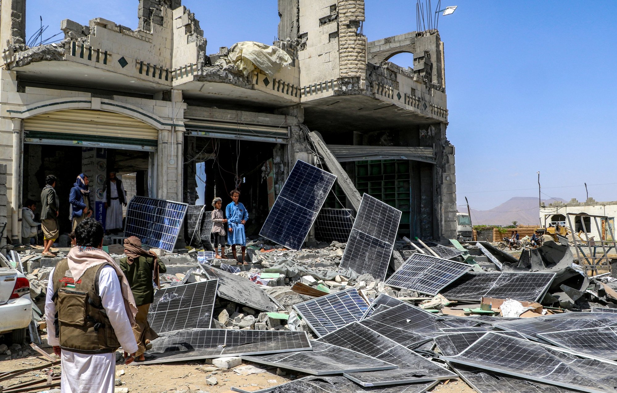 Destruction : bâtiment effondré, débris et panneaux solaires éparpillés autour.