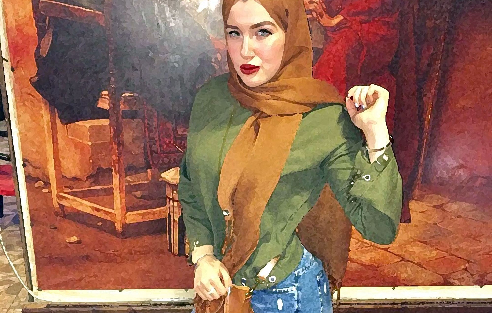 L'image montre une jeune femme se tenant debout dans ce qui semble être un café ou un restaurant. Elle porte un hijab marron ainsi qu'une chemise verte et un pantalon en jean ajusté. Ses chaussures sont marron. On peut observer un décor coloré derrière elle, représentant des personnages. La femme adopte une pose confiante, avec une main sur la hanche et un sourire sur le visage.
