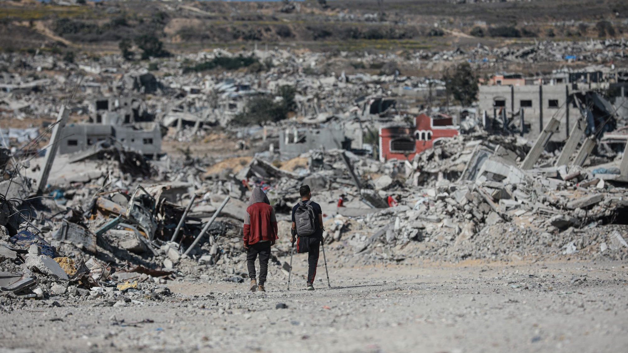 Deux personnes marchent dans un paysage de destruction, entourées de débris.