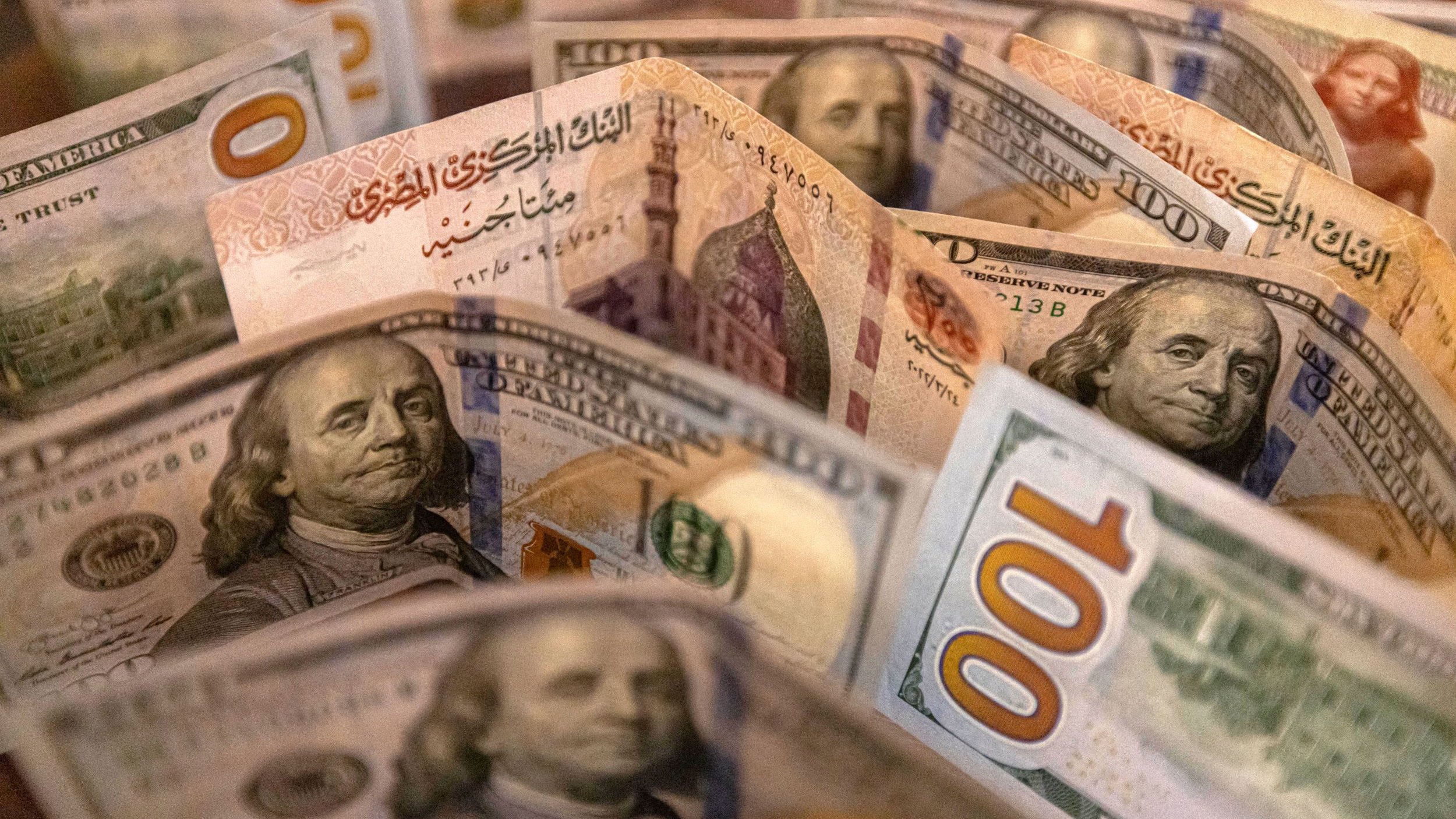 L'image montre un assortiment de billets de banque, probablement des dollars américains. On peut voir plusieurs billets de 100 dollars, avec des illustrations de Benjamin Franklin, ainsi que d'autres détails de la conception des billets. Les billets sont disposés de manière à créer une sorte de fan, mettant en évidence les différentes couleurs et motifs.