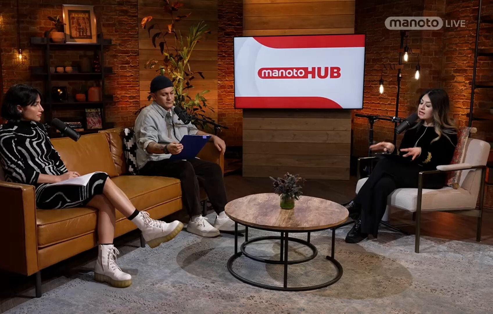 Trois personnes discutent dans un salon moderne, avec un écran au fond.