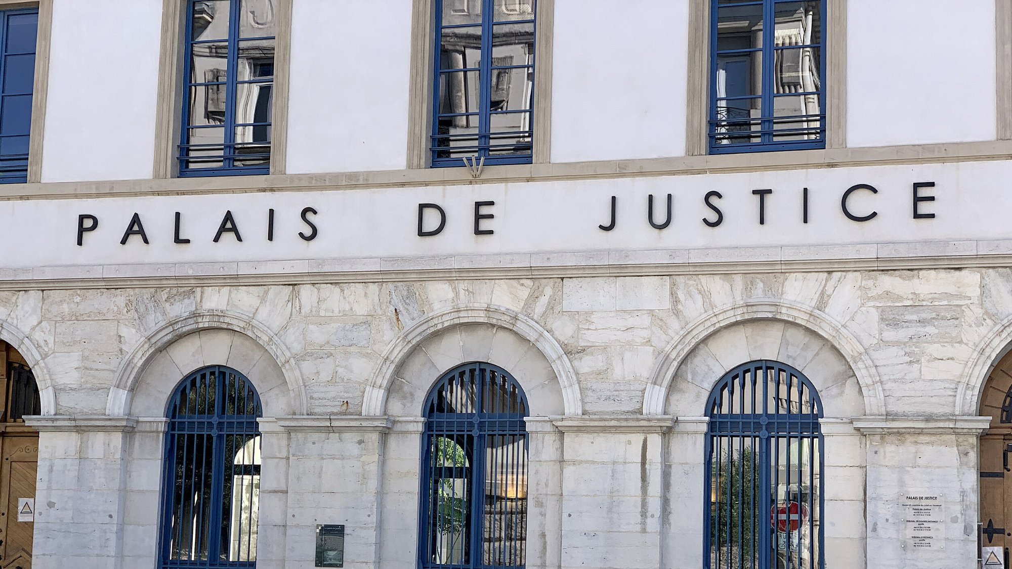 Façade d'un bâtiment imposant avec l'inscription "Palais de Justice" et des fenêtres à arcs.