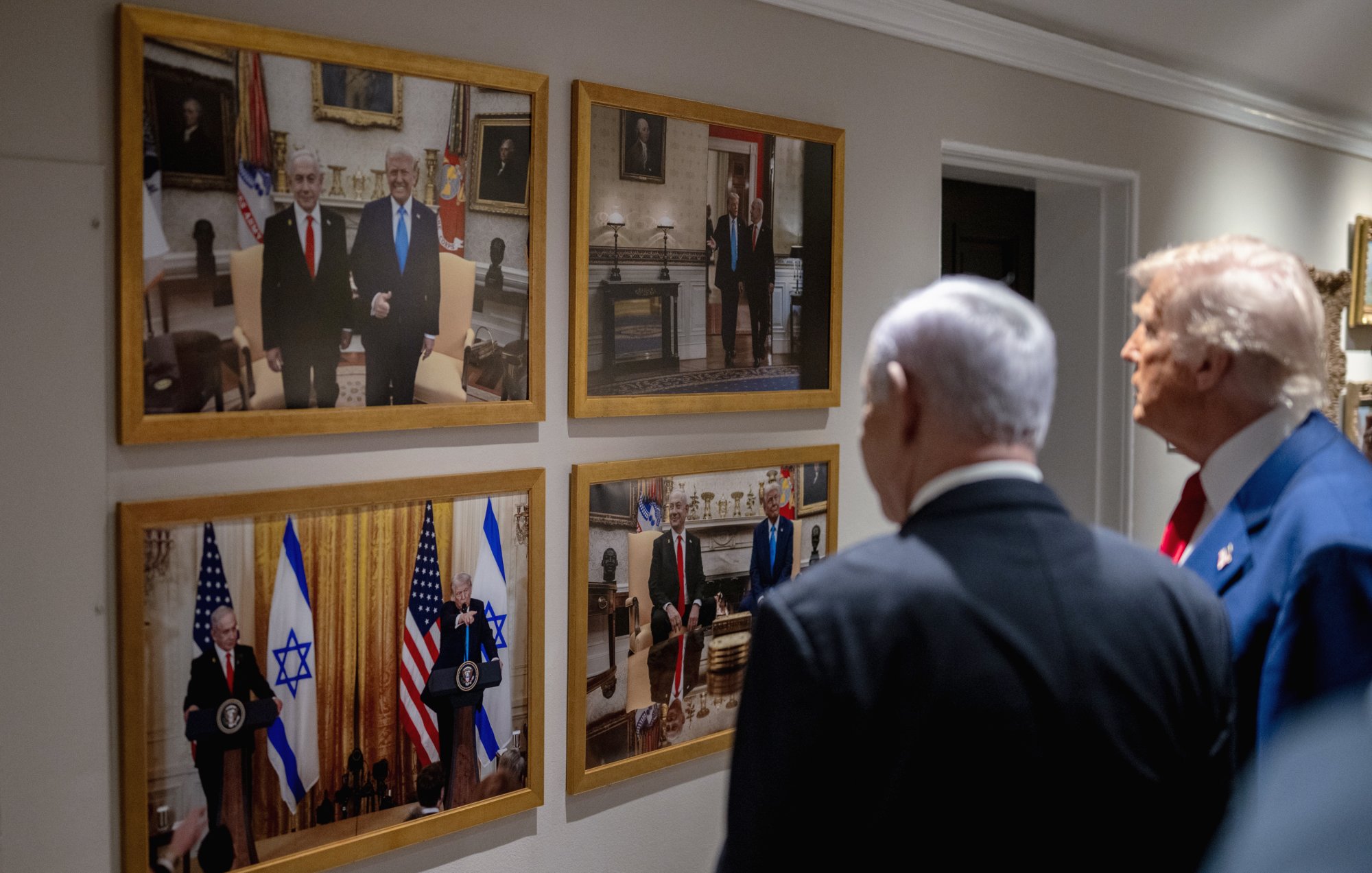 Des hommes politiques regardent des photos accrochées au mur, représentant des rencontres officielles.