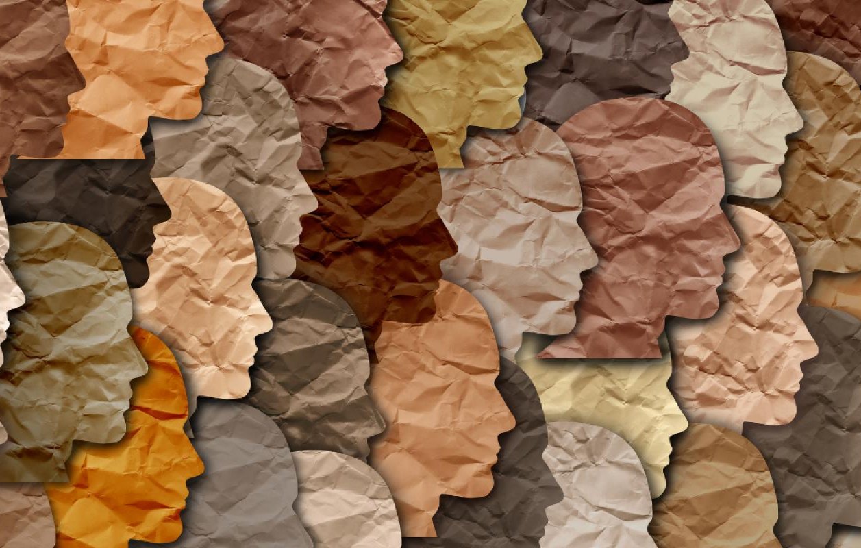 L'image représente une mosaïque de profils humains en silhouettes, créés à partir de papier froissé aux différentes nuances de couleurs de peau. Les teintes varient du beige clair au brun foncé, illustrant la diversité des origines humaines. La texture froissée ajoute une dimension tactile à l'œuvre, suggérant une approche artistique qui évoque à la fois l'unité et la diversité.