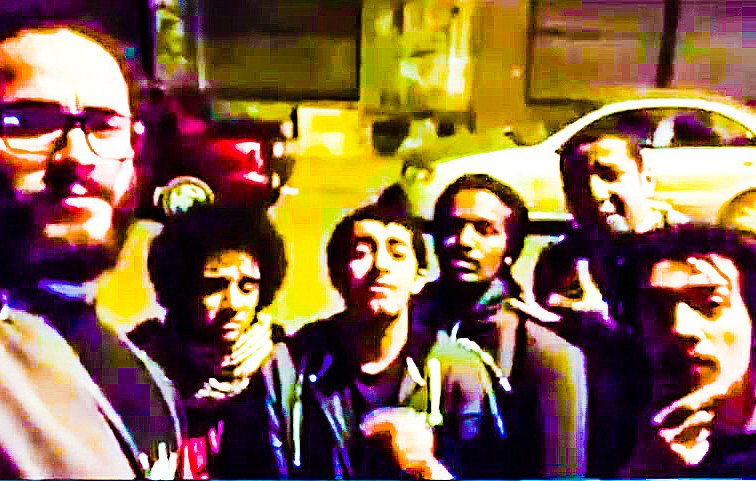 L'image montre un groupe de six personnes posant ensemble devant une voiture garée. Ils semblent être de jeunes adultes, certains portant des lunettes ou ayant des cheveux frisés. L'ambiance est détendue et amicale, et la photo semble avoir été prise de nuit, avec un éclairage un peu faible. La scène donne une impression de camaraderie et de convivialité entre les individus.