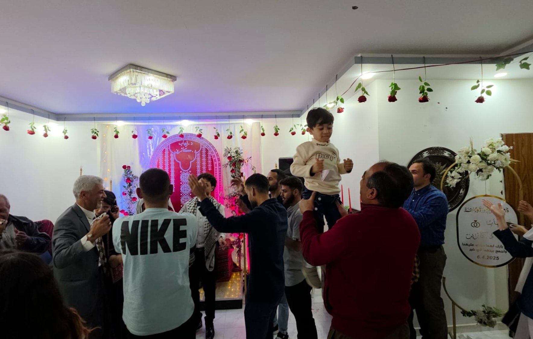 Fête joyeuse avec des gens dansant, décorations florales et un enfant porté.