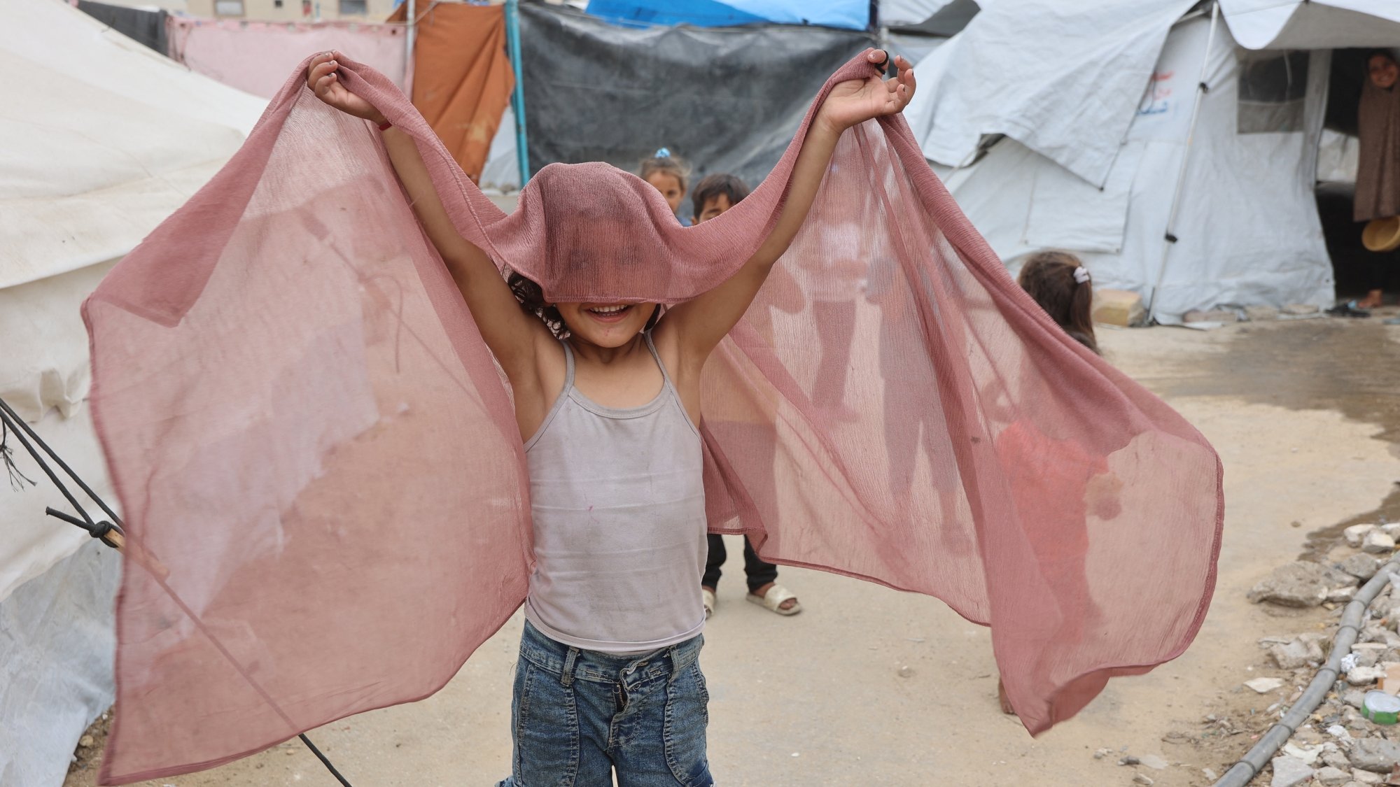 Enfant joyeux tenant un tissu léger, jouant près de tentes.