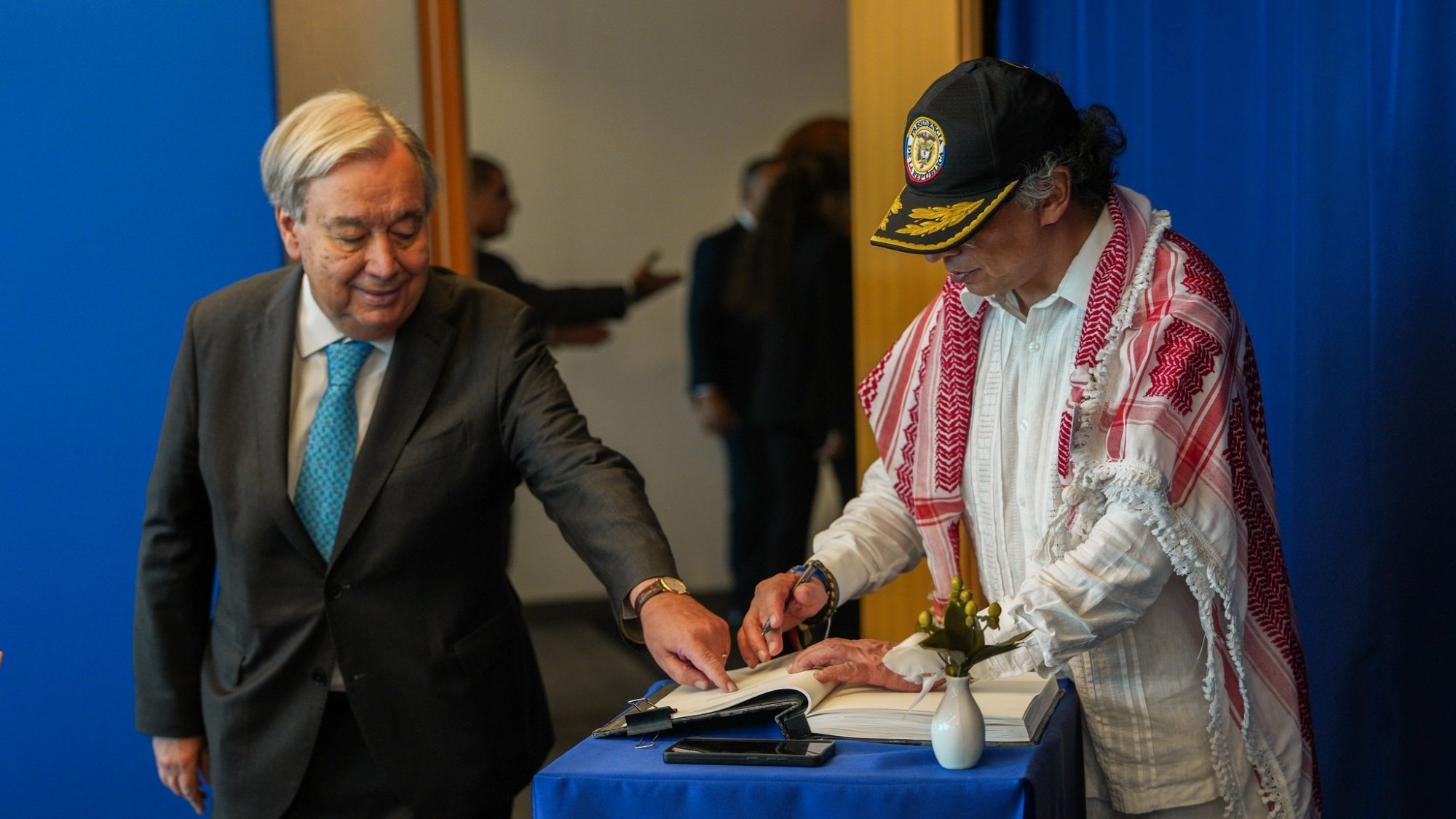 Deux hommes, l'un en costume et l'autre en tenue traditionnelle, signent un livre ensemble.