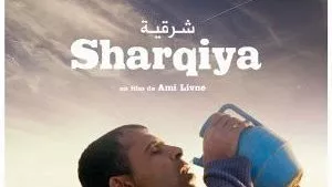 L'image représente une scène d'un film intitulé "Sharqiya", réalisé par Ami Livne. On y voit un homme portant un pot en plastique, semblant s'hydrater en plein air. Le décor suggère un paysage rural, avec quelques animaux en arrière-plan. L'expression de l'homme pourrait évoquer une recherche de répit ou un moment de pause dans un environnement quotidien.