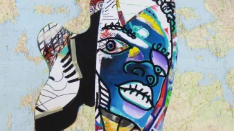 Cette image présente une œuvre d'art colorée et abstraite. Elle combine des formes humaines stylisées et des motifs graphiques, avec des couleurs vives comme le bleu, le rouge, le noir et le jaune. En arrière-plan, on peut voir une carte du monde, ce qui ajoute une dimension géographique à la composition. Les traits du visage dessiné semblent expressifs, avec des lignes fluides et des éléments graphiques qui renforcent le caractère artistique de l'œuvre. L'ensemble évoque un mélange de cultures et d'identités.