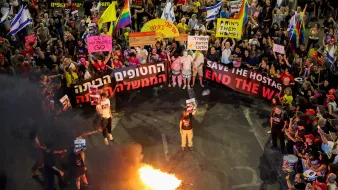 Manifestation animée avec des drapeaux et des pancartes, feu visible au centre.