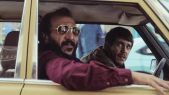 Deux hommes dans une voiture, l'un avec des lunettes de soleil, l'autre semble inquiet.