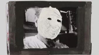 L'image présente une photographie en noir et blanc d'un visage, mais celui-ci est recouvert d'une peinture blanche qui dissimule complètement les traits du visage. La photo est encadrée par une bordure noire, ce qui attire l'attention sur le contraste entre le fond sombre et la surface blanche du visage. Ce traitement artistique crée une atmosphère intrigante et mystérieuse, en poussant le spectateur à réfléchir sur l'identité et l'anonymat.