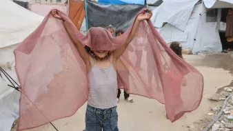 Enfant joyeux tenant un tissu léger, jouant près de tentes.