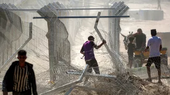 Des hommes manipulent des barbelés près d'une clôture dans un environnement poussiéreux.