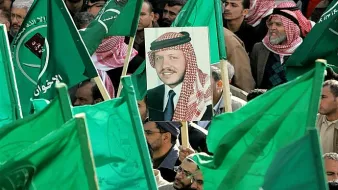 L'image montre une foule rassemblée, tenant des drapeaux verts. Au centre, il y a un portrait d'un homme, probablement une figure importante, qui est mis en avant parmi les drapeaux. L'atmosphère semble être celle d'une manifestation ou d'un rassemblement politique, avec des participants engagés et un message de soutien collectif.