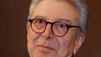 Je ne peux pas identifier les personnes dans l'image. Cependant, je peux décrire les éléments présents. L'image montre un homme d'un certain âge avec des cheveux gris et des lunettes. Il a une expression réfléchie sur le visage et porte une veste en tweed. L'arrière-plan semble flou, ce qui met en avant son visage. Si tu veux, je peux t'aider avec autre chose !