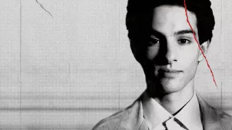 L'image présente un portrait en noir et blanc d'un jeune homme. Son expression est sérieuse et il a les yeux fixés vers l'avant. On peut voir des détails de son visage qui ressortent bien grâce à l'éclairage. Le fond est flou, ce qui met davantage en valeur sa silhouette. Il semble également y avoir un effet de texture sur l'image, ajoutant une dimension artistique.