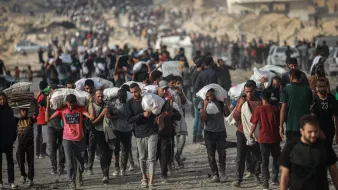 Des personnes marchent en masse, portant des charges sur leurs épaules, dans un environnement difficile.