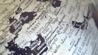 L'image montre une carte géographique en noir et blanc de la région du Moyen-Orient. On y voit des pays tels que la Turquie, l'Iran, l'Irak, la Syrie et l'Arabie Saoudite, ainsi que des villes importantes comme Bagdad et Bassora. Les noms des pays et des villes sont clairement inscrits, offrant une perspective sur la géographie de cette zone. La carte semble ancienne, ce qui lui donne un aspect vintage.